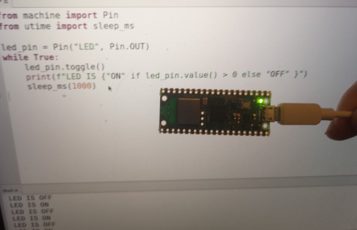 Raspberry pi pico is held via its USB cable with its embedded led turned on. On the background Thonny IDE is visible with the python code that runs to achieve the blinking effect